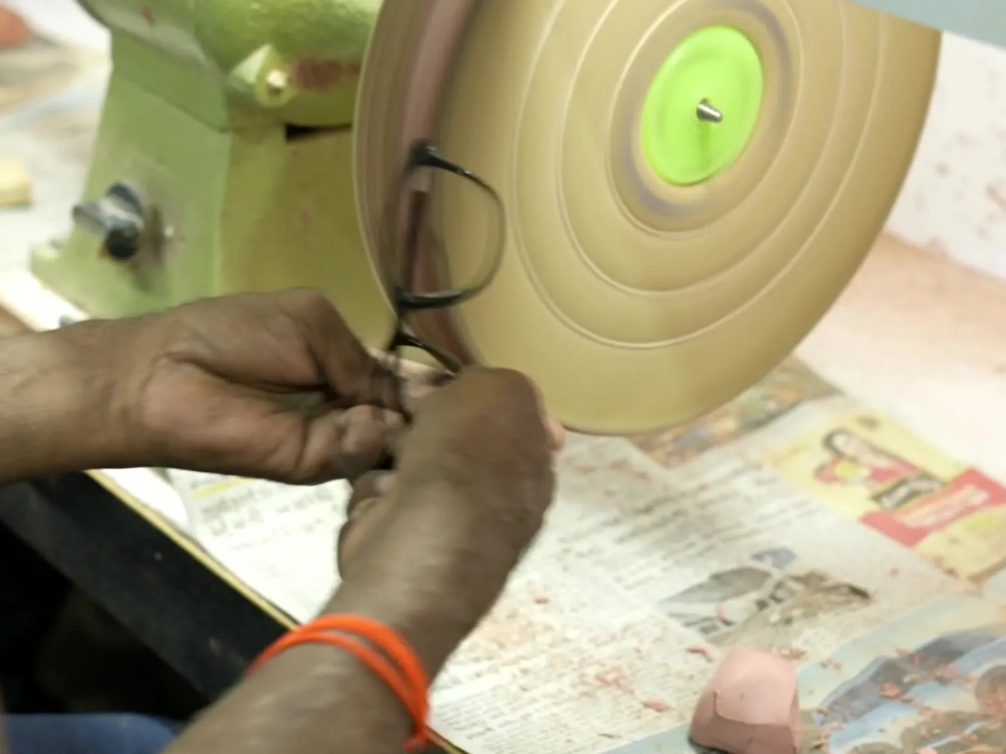 A worker finishing the edge of an acetate frame front against a polishing wheel at the Rushabh Trading Company workshop